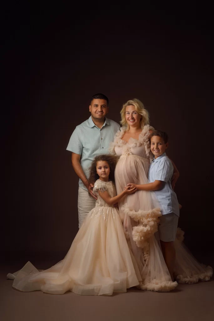 A happy family at a maternity photoshoot, with the mother cradling her baby bump and everyone beaming with joy.